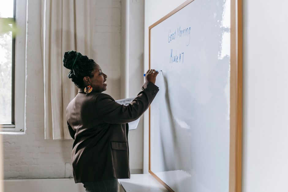 Side view of smiling African American woman writing on whiteboard standing in modern school classroom